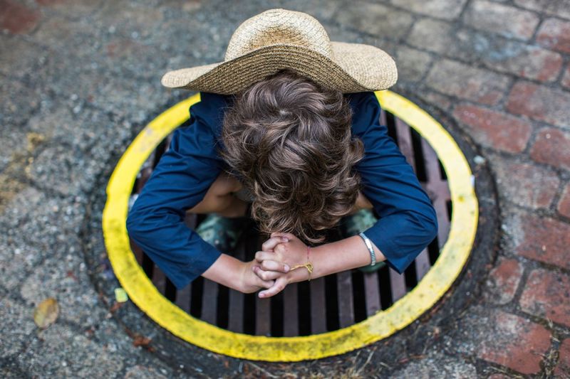 High angle view of boy wearing hat while crouching on manhole