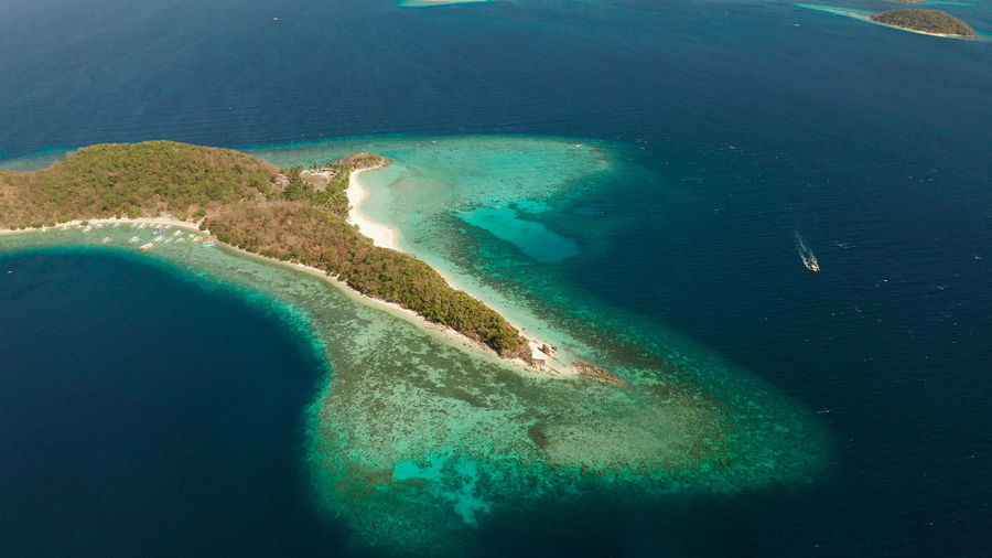 Aerial drone island in blue lagoon with sandy beach and coral reef. malcapuya, philippines, palawan.