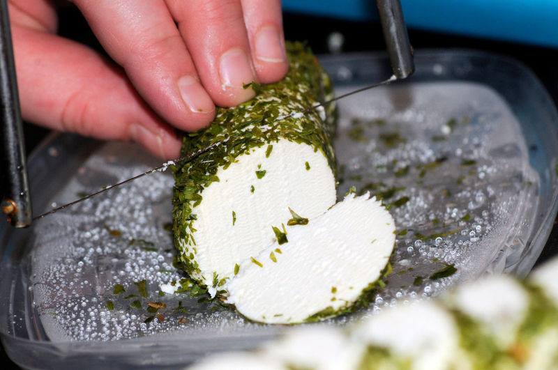 Cutting fresh cream cheese rolled in green herbs into pieces