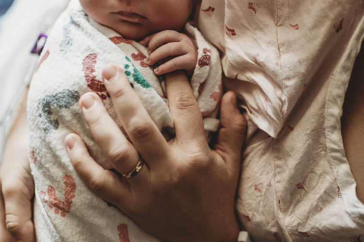 Macro overhead view of mother holding newborn boy's fingers in hospita