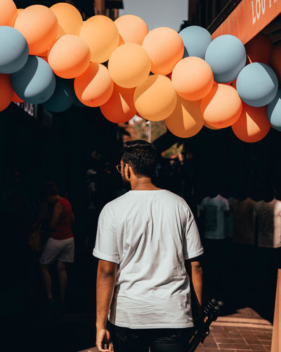 Rear view of man walking towards balloons on footpath