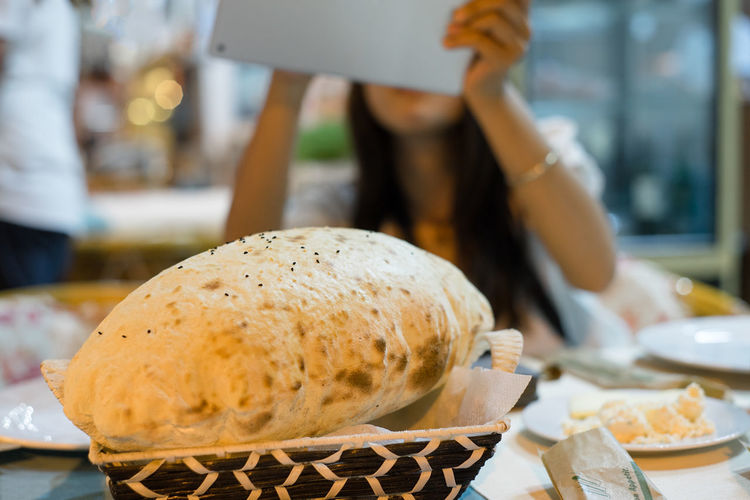 Close-up of puffed roti with woman using technology in background