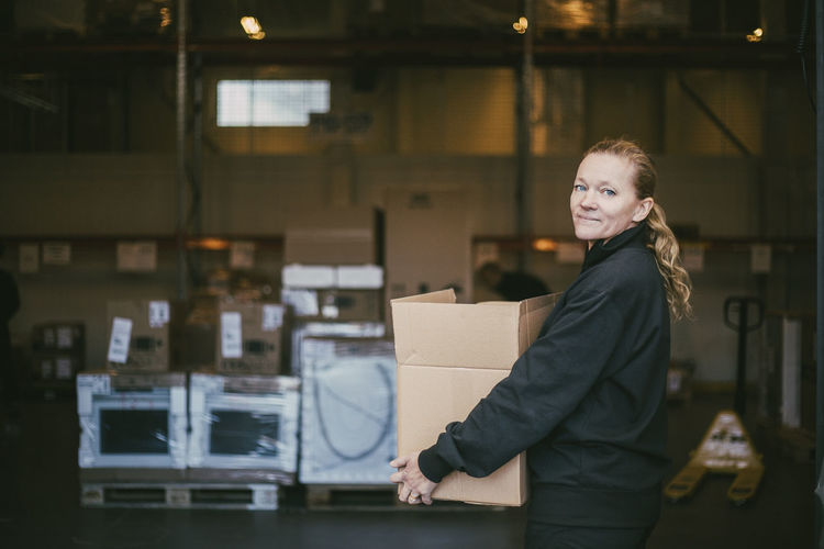 Mature businesswoman carrying box container in logistics warehouse