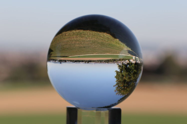 Close-up of crystal ball on glass against sky