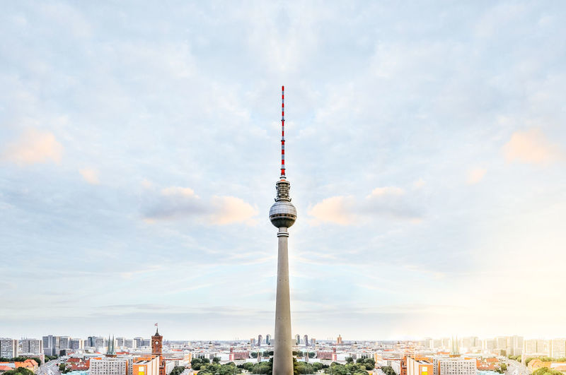 Fernsehturm tower and buildings against cloudy sky in city