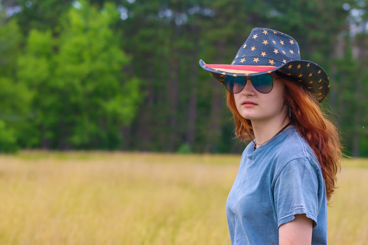 Country girl on a prairie wearing aviator sunglasses and an american flag hat.