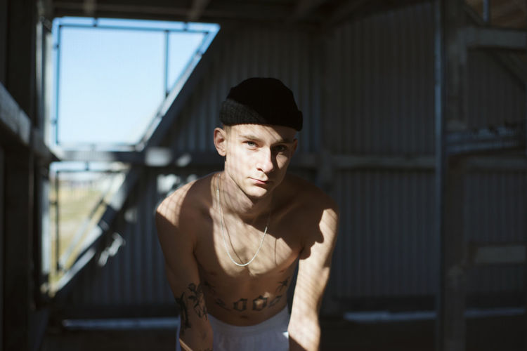 Portrait of shirtless young man wearing knit hat standing indoors