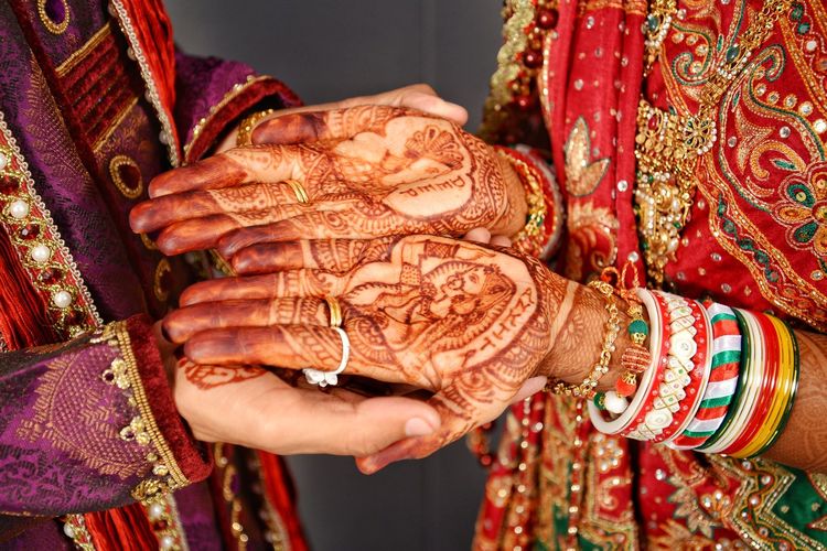 Midsection of groom holding bride hands with henna tattoo