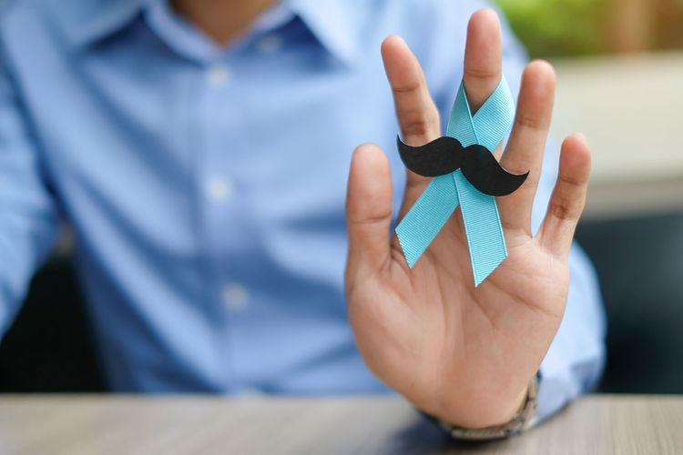 Midsection of man holding blue ribbon with mustache