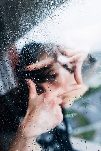 Close-up portrait of woman seen through wet window in rainy season