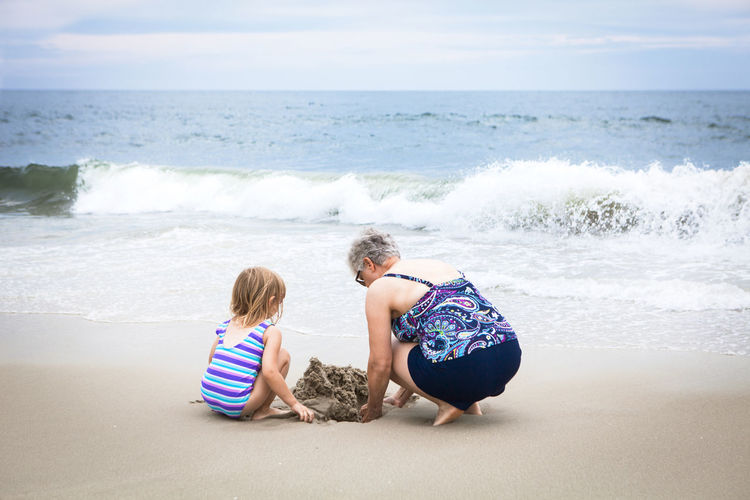 Rear view of grandmother with granddaughter digging sand at beach