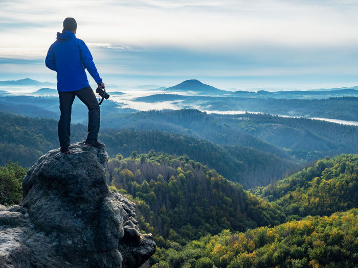 Camera in the hand of man standing on rock and looking into landscape. photographer and camera