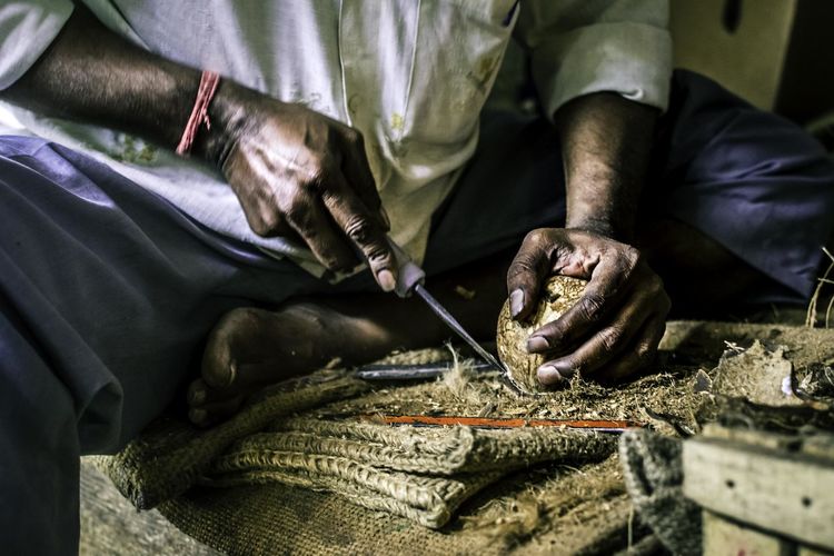 Midsection of man cutting coconut on burlap