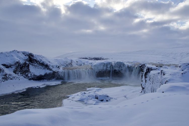 Scenic view of snowcapped mountains with waterfalls against sky