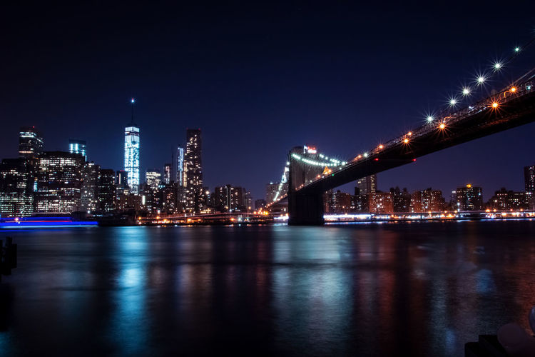 Illuminated bridge over river with buildings in background at night