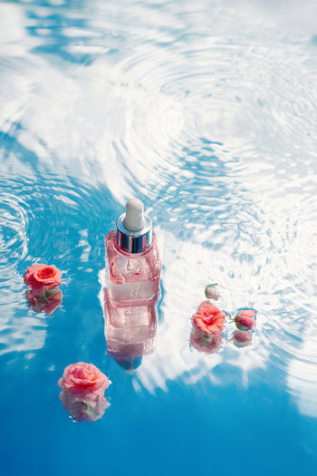 Pink serum bottle in blue water with flowers, texture of ripples and waves