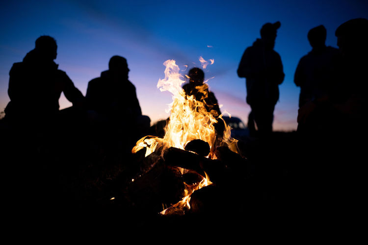 A group of friends gathered around the fire at night