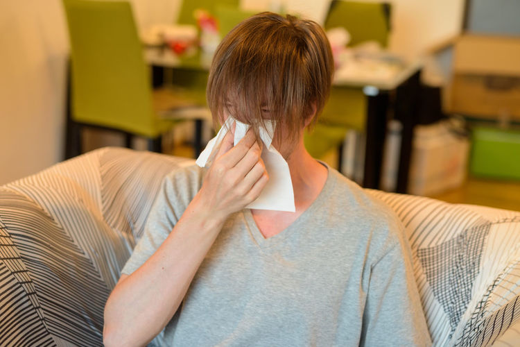 Man sneezing while sitting on sofa at home