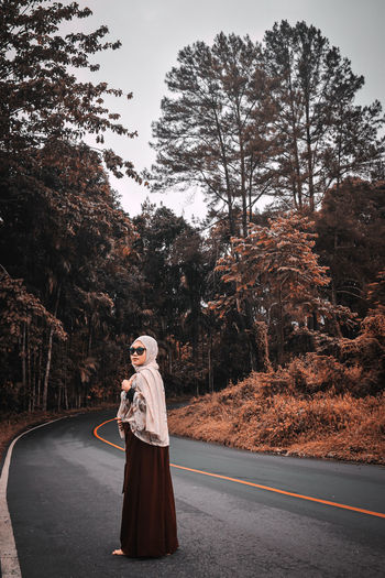 Full length of woman standing on road amidst trees