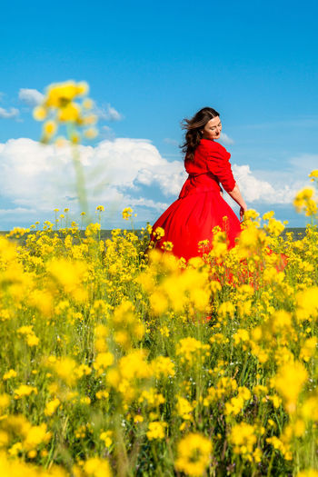 Rear view of woman standing amidst yellow flowering plants on field
