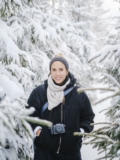 Portrait of woman with camera standing in snowy forest