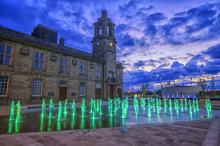 Illuminated human fountains outside historic building at dusk