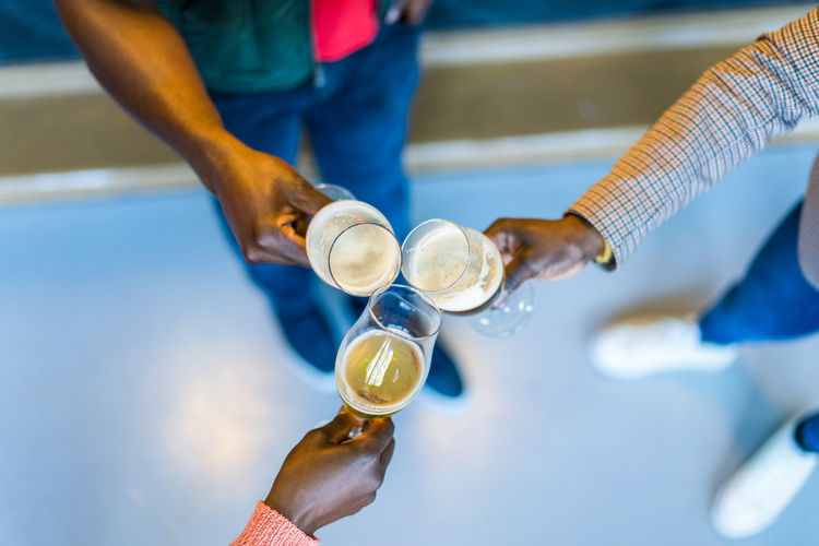 From above group of unrecognizable african american happy friends clinking glasses with beer while enjoying weekend together in bar