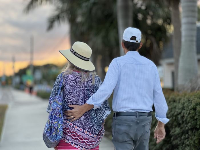 Rear view of senior couple in blue walking on sidewalk under palm trees at sunrise. portrait.