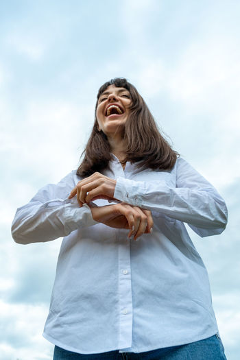 Low angle view of smiling woman standing against sky