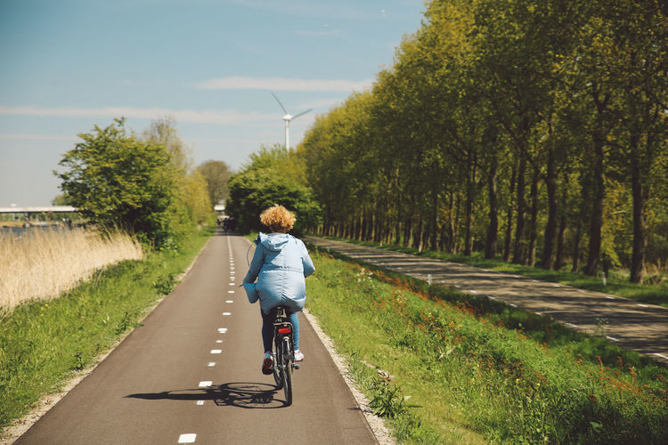 Rear view of woman riding bicycle on road during sunny day