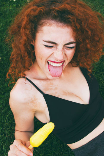 Woman sticking out tongue while having popsicle on grassy field