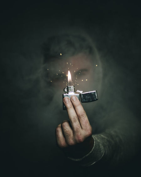 Close-up of man holding burning cigarette lighter amidst smoke