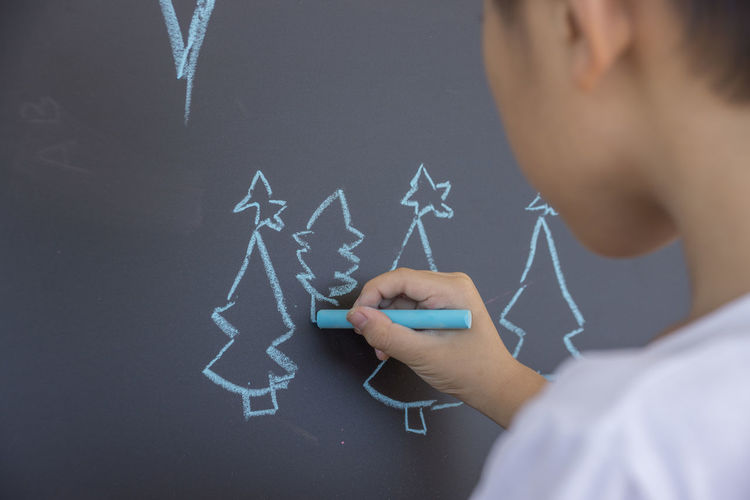 Close-up of boy drawing christmas tree on blackboard