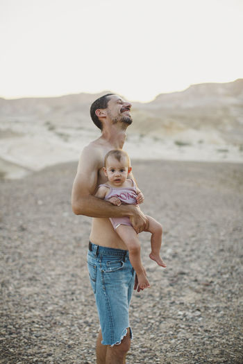 A father laughing while holding his baby girl in the desert
