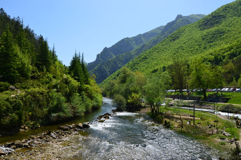 Scenic view of river by green mountains against clear sky