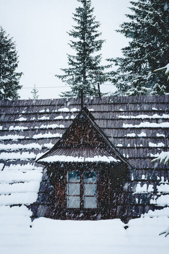 Snow covered house and trees against sky