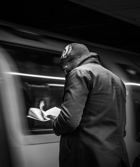 Man reading book while standing at railroad station platform