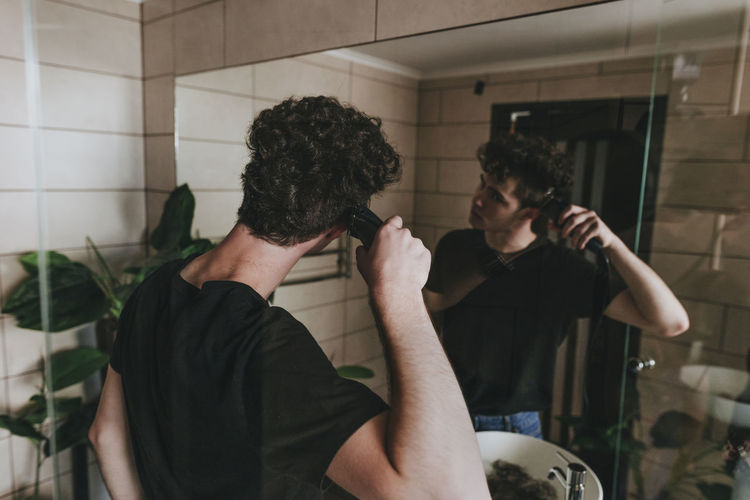 Man looking in mirror and cutting his own hair at home