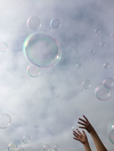 Low angle view of cropped hands and bubbles against sky