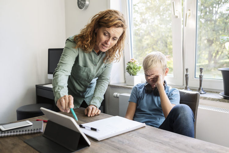 Mother teaching son on digital tablet at home