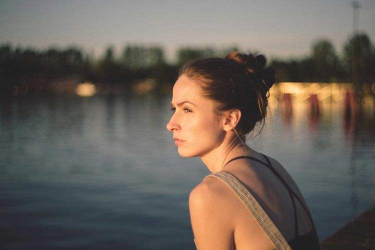 Portrait of young woman looking away while standing in lake during sunset