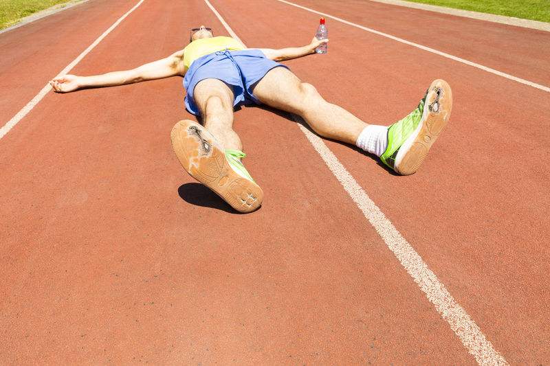 Mid adult man lying on running track during sunny day