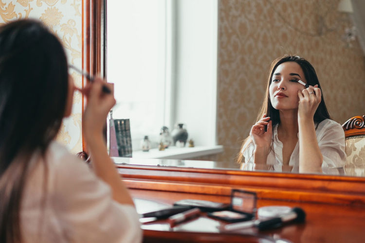 Young woman doing make-up while looking at mirror