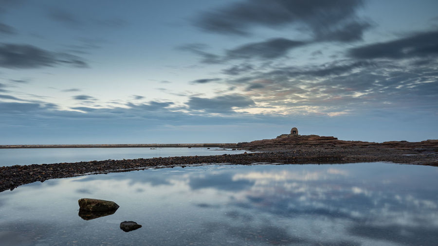 Old building on the coast at blue hour with clouds reflected in a rock pool