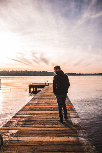 Man standing on pier over lake against sky