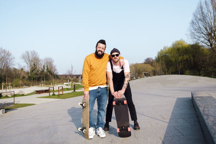 Friends standing with skateboard in skatepark on sunny day