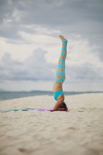 Full length of woman doing headstand on beach against sky