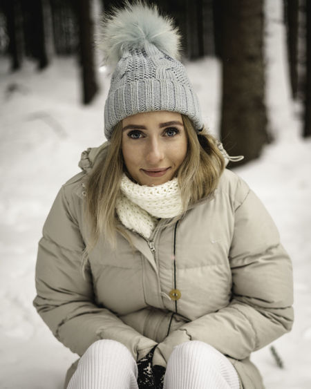 Portrait of young woman sitting on snow covered land during winter