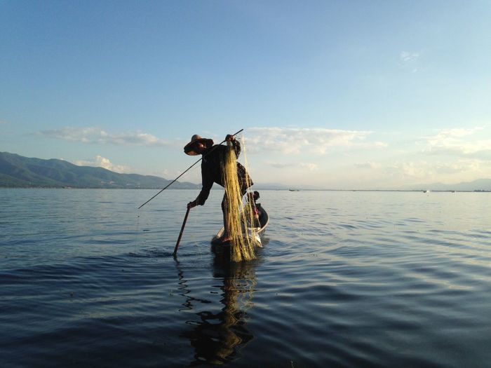 Fisherman fishing on boat in sea against blue sky
