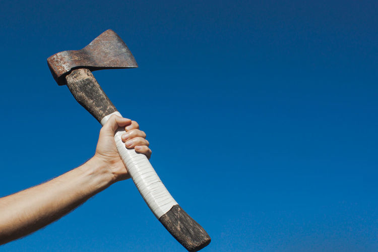 A european man hand tightens a white handle of an old ax with the sky on the background
